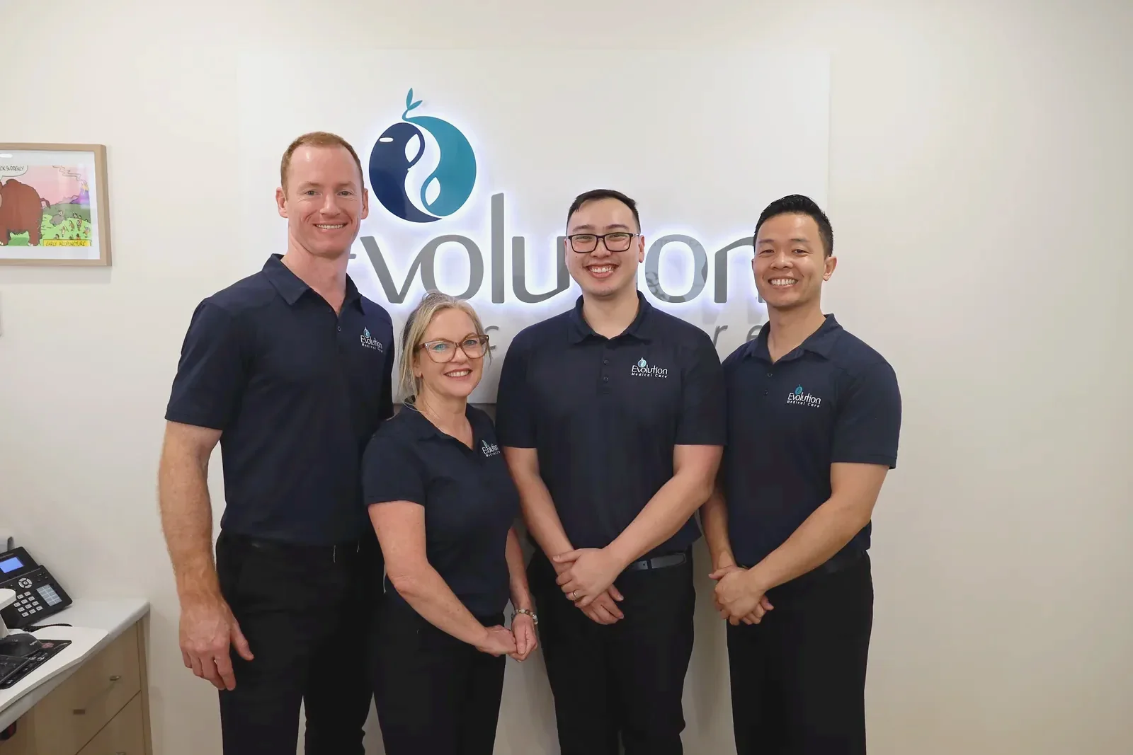 Four staff in navy uniforms stand together smiling beneath the lit Evolution Medical Care logo sign.