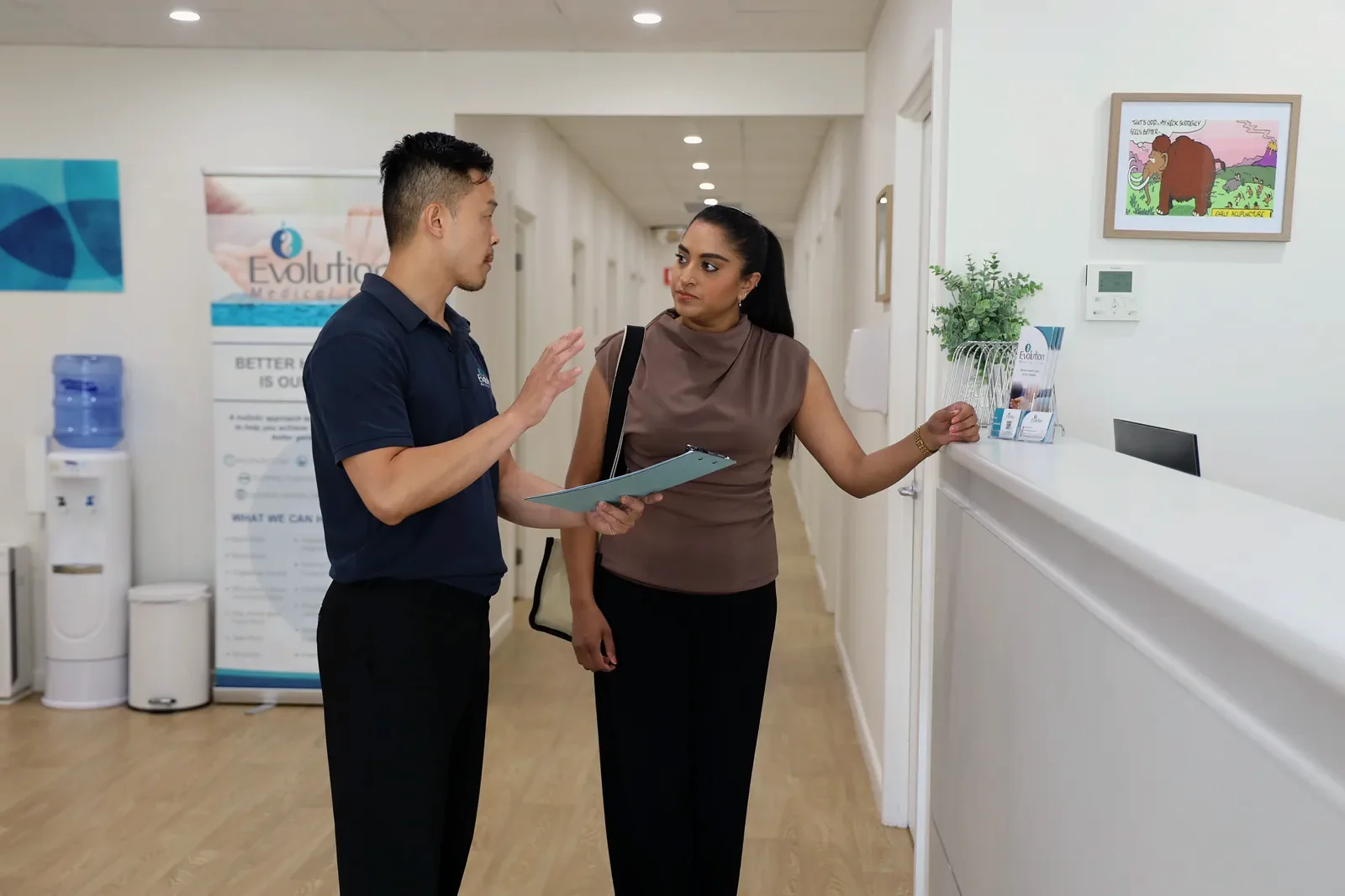 A practitioner holding a folder talks with a woman in the clinic hallway beside an Evolution Medical Care banner.